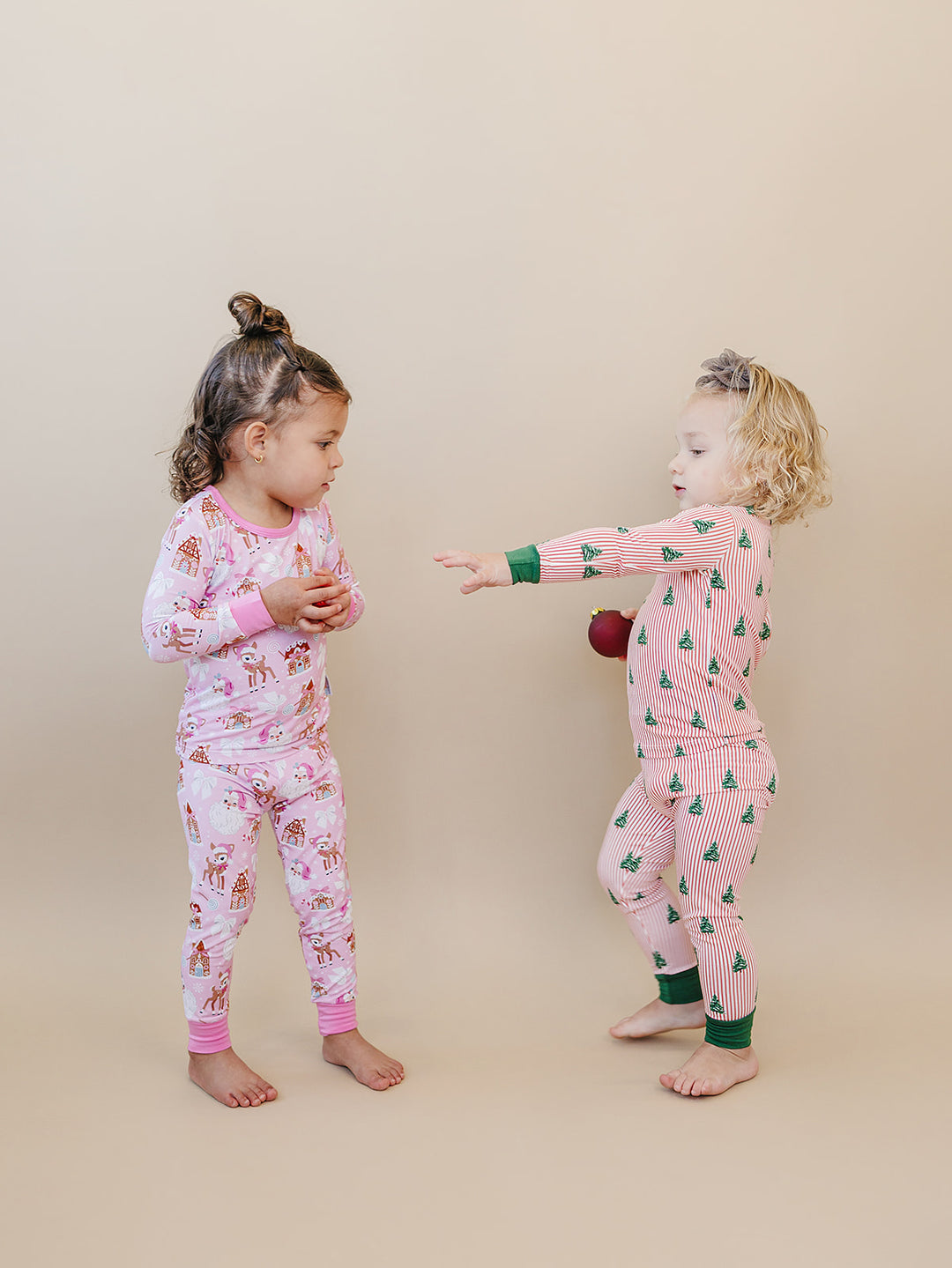 Two toddlers facing each other in Pink Christmas and Magical Trees holiday pajamas.