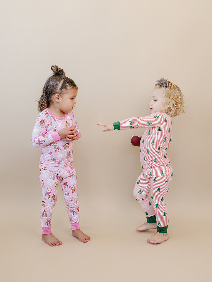 Two toddlers facing each other in Pink Christmas and Magical Trees holiday pajamas.