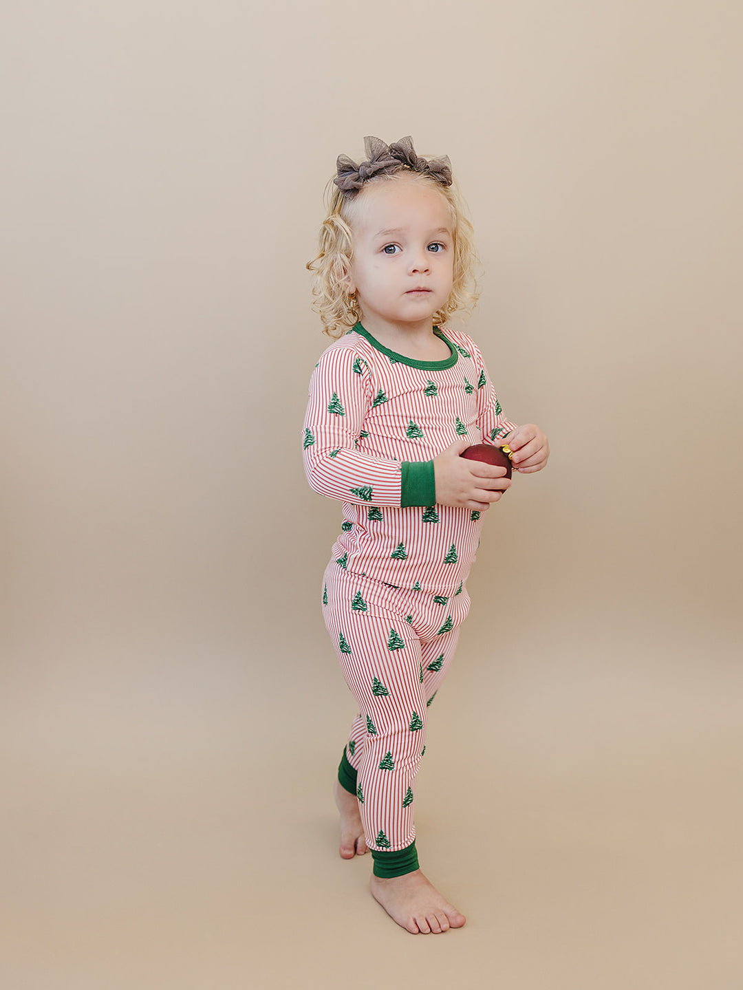 Toddler turned sideways in Magical Trees striped Christmas pajamas with green cuffs.