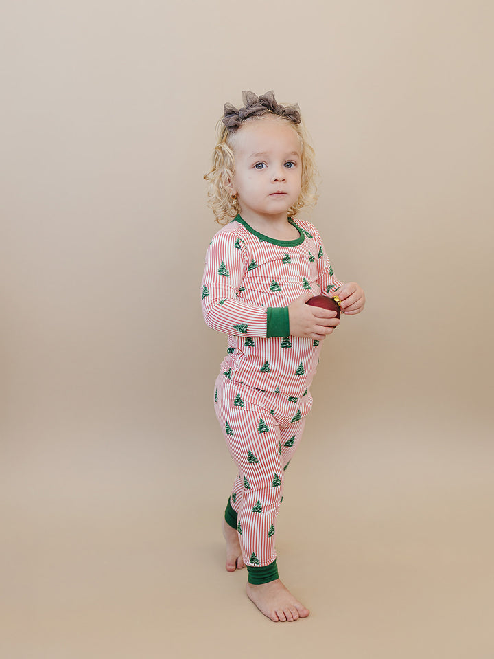 Toddler turned sideways in Magical Trees striped Christmas pajamas with green cuffs.