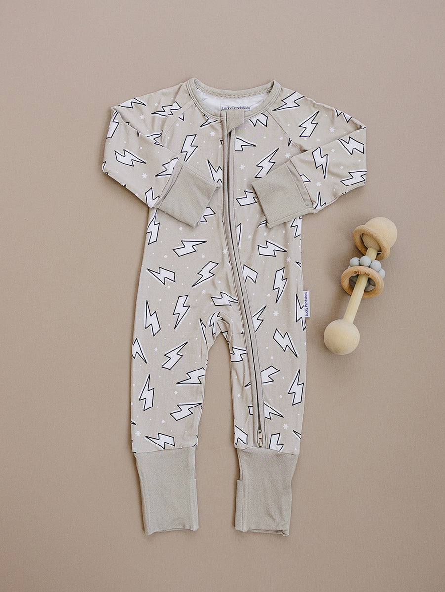 Latte Bolts bamboo zip romper laid flat beside a wooden teething toy, showing the complete lightning bolt print.