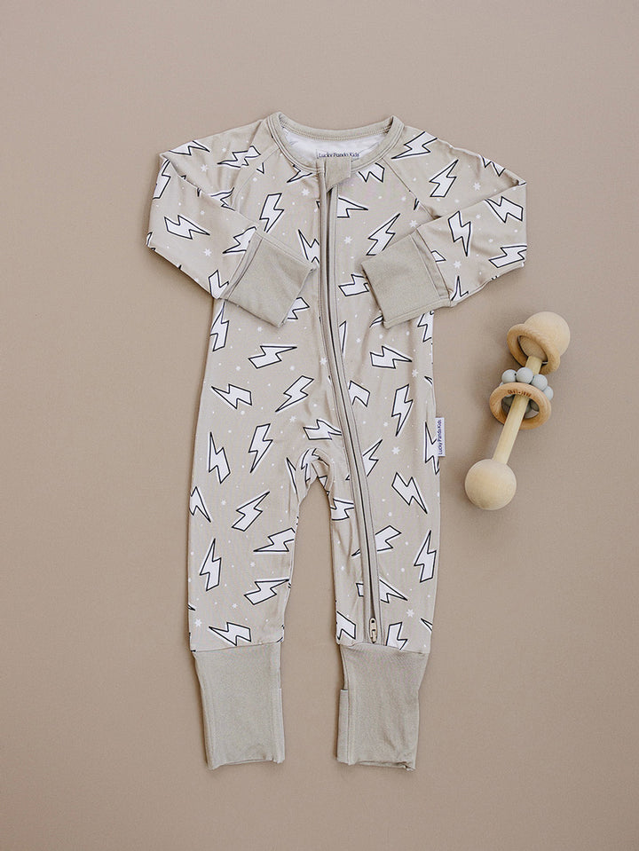 Latte Bolts bamboo zip romper laid flat beside a wooden teething toy, showing the complete lightning bolt print.