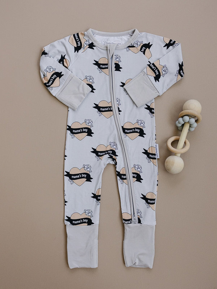 Mama’s Boy long-sleeve bamboo zip romper with beige hearts and black banners displayed flat.