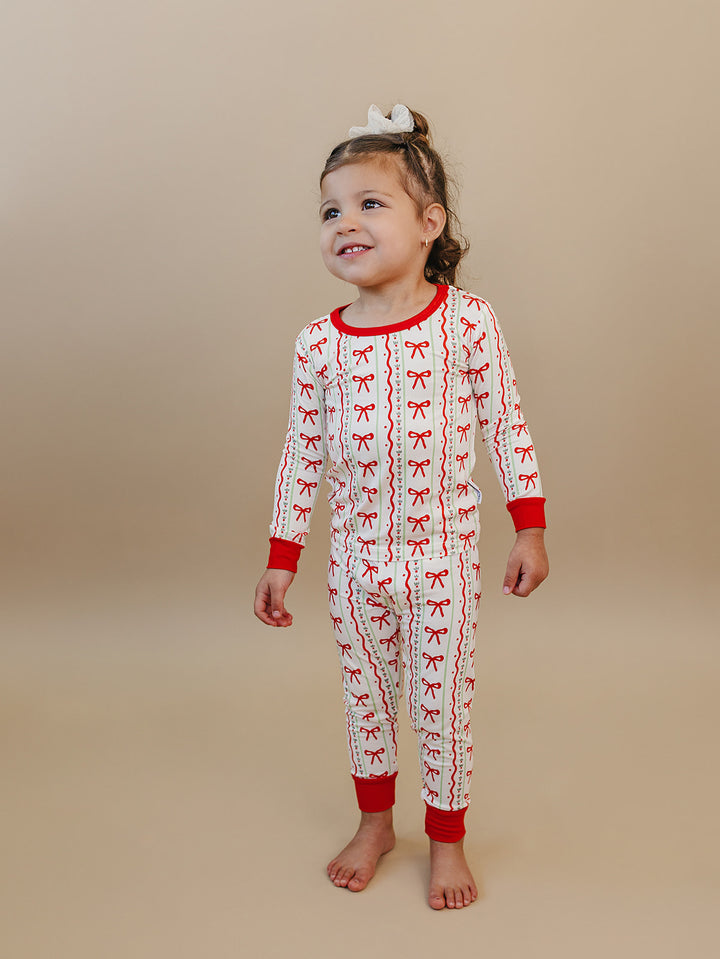 Toddler looking to the side in Christmas Bows pajamas with a cream background and red cuffs.