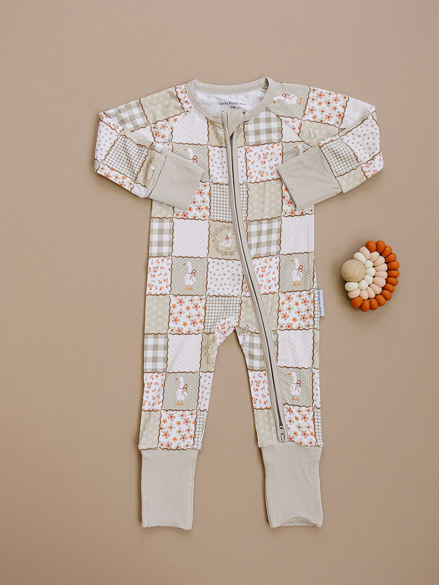 Cottage Goose bamboo zip romper laid flat beside a wooden teething toy, showing the complete patchwork print.