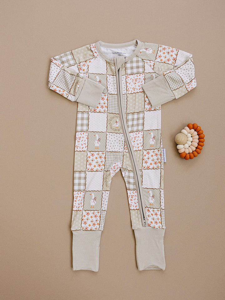 Cottage Goose bamboo zip romper laid flat beside a wooden teething toy, showing the complete patchwork print.