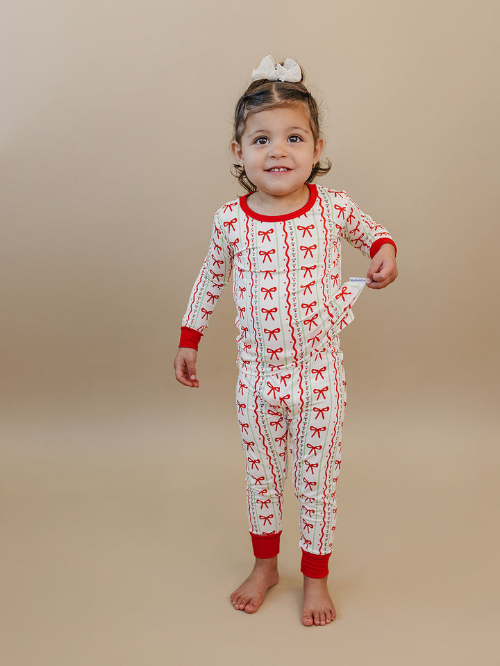 Toddler standing barefoot in Christmas Bows two piece pajamas with red wrist and ankle cuffs.