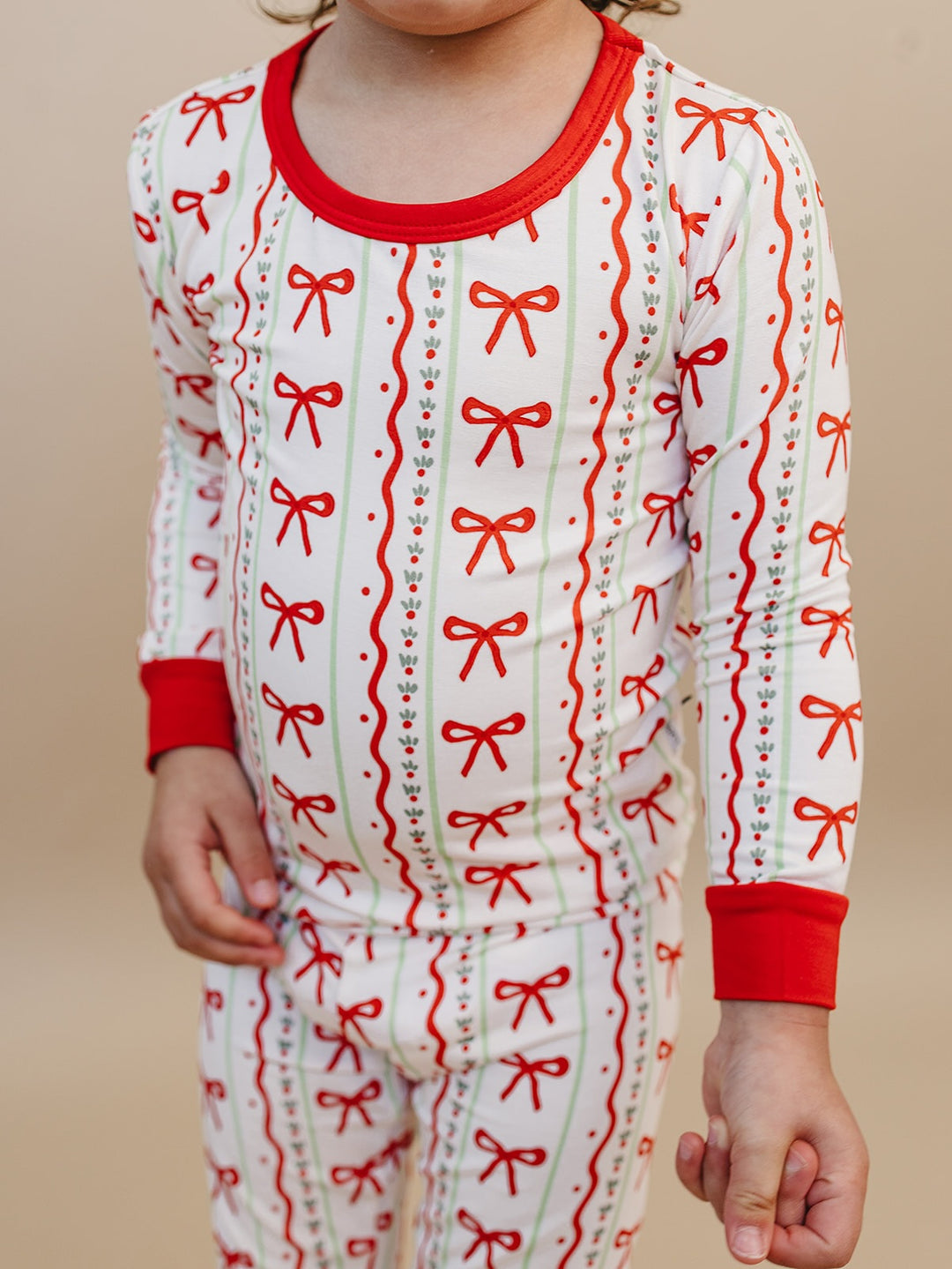Detail of a child wearing Christmas Bows pajamas, showing the red neckline, wrist cuffs and bow print.