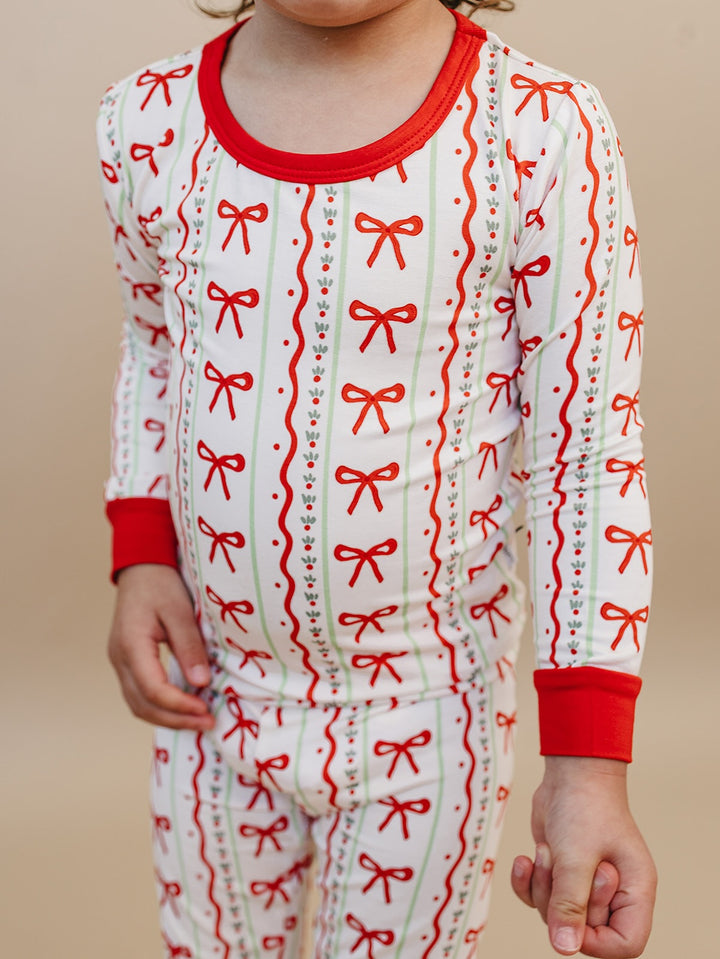 Detail of a child wearing Christmas Bows pajamas, showing the red neckline, wrist cuffs and bow print.