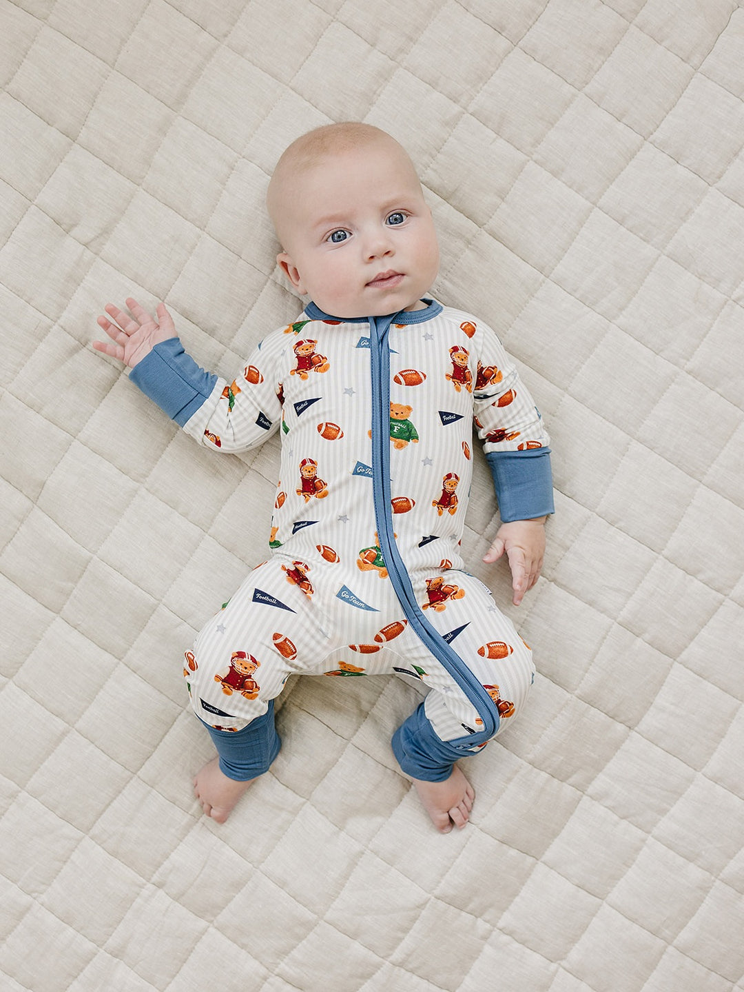 Baby lying on a cream quilted mat in the Touchdown Teddy bamboo zip romper.