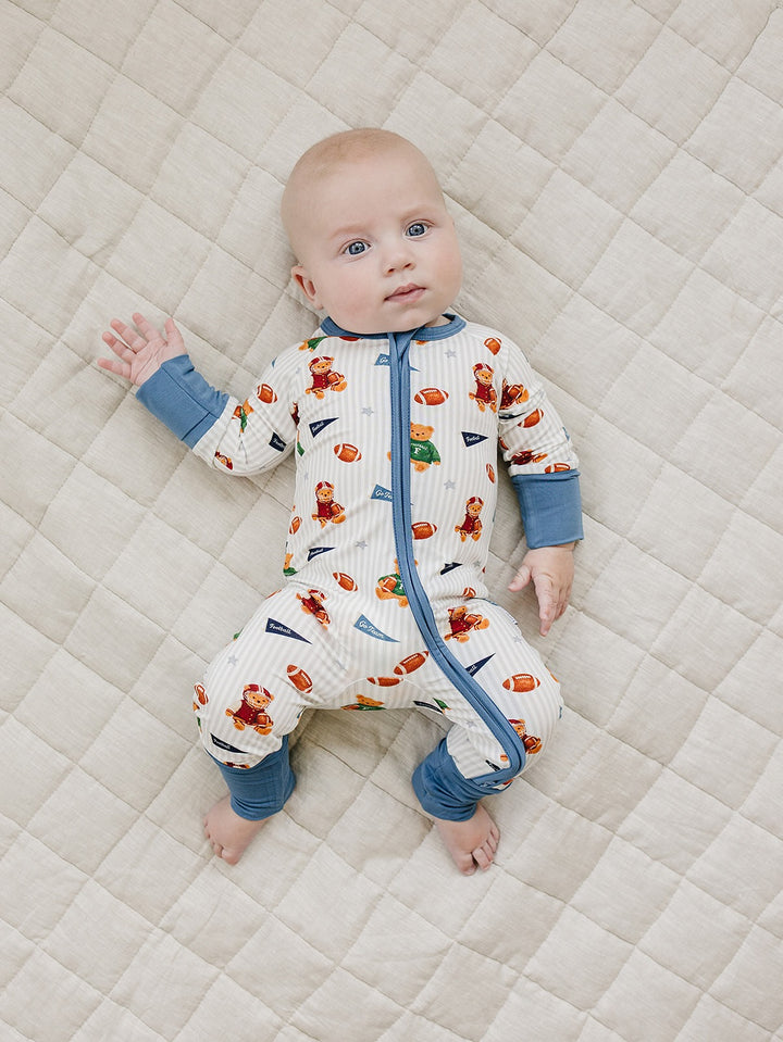 Baby lying on a cream quilted mat in the Touchdown Teddy bamboo zip romper.