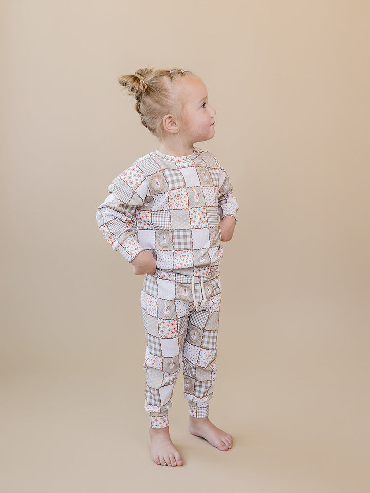 Full-length back view of a toddler girl wearing the Cottage Goose jogger set against a beige background.