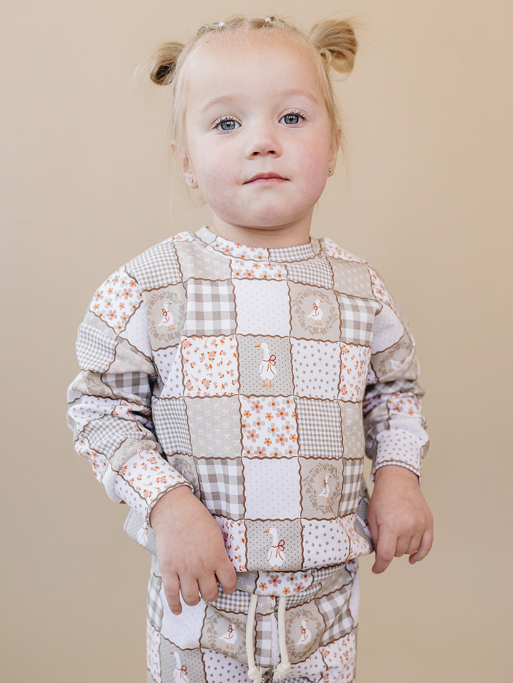 Toddler girl modeling the Cottage Goose cotton jogger set from the front against a warm beige studio background.