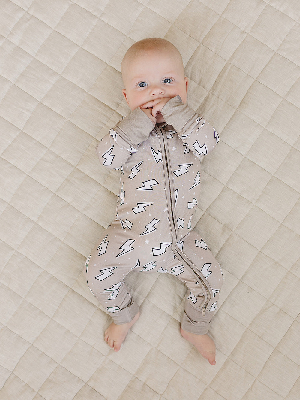 Full-body view of a baby lying on a quilt in the Latte Bolts bamboo zip romper.