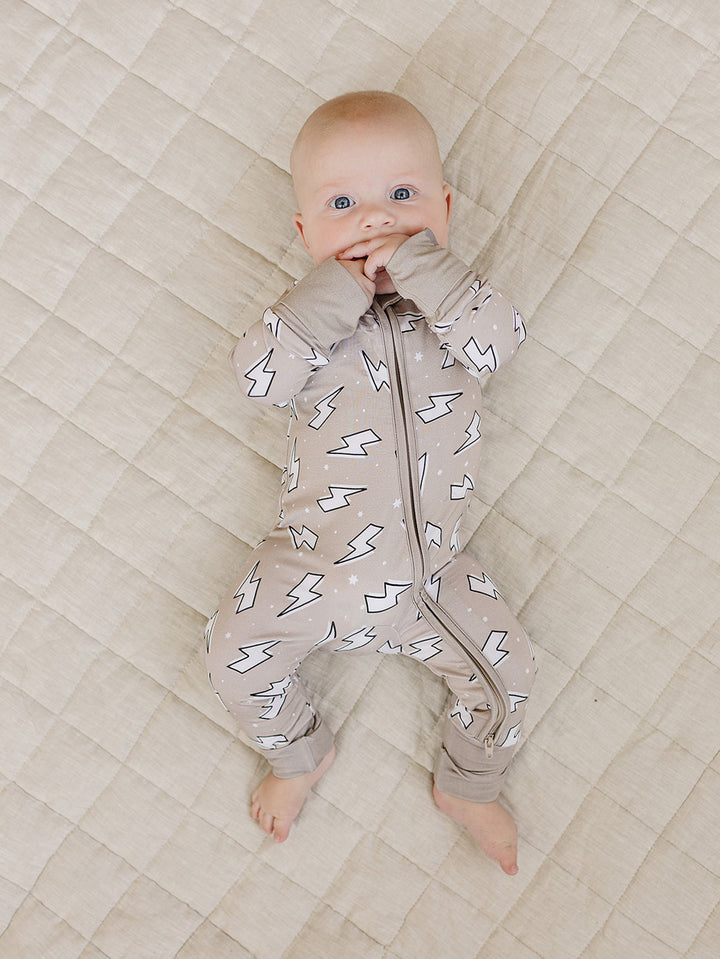 Full-body view of a baby lying on a quilt in the Latte Bolts bamboo zip romper.