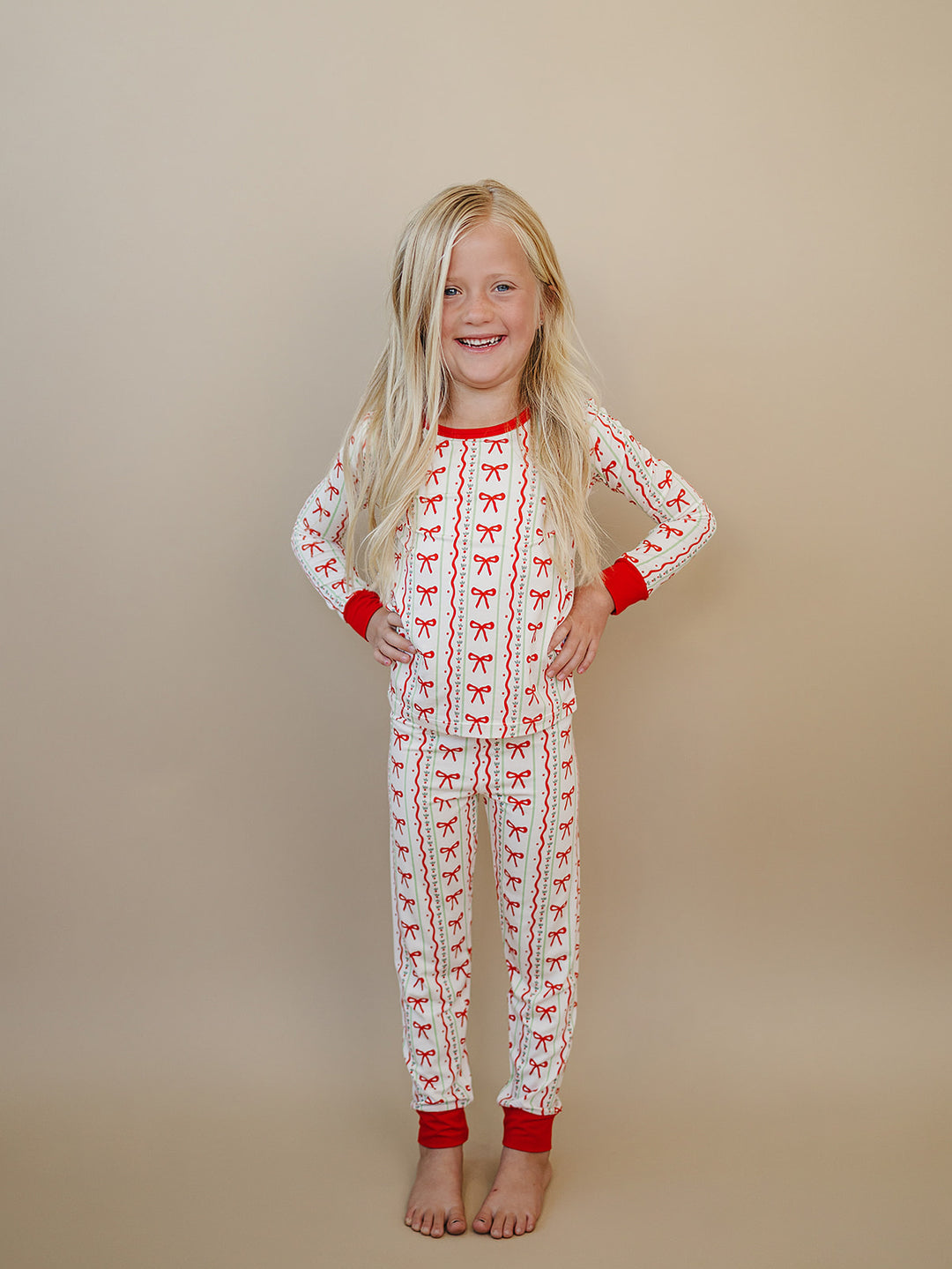 Child standing barefoot with hands on hips in the Christmas Bows long sleeve top and matching pants.