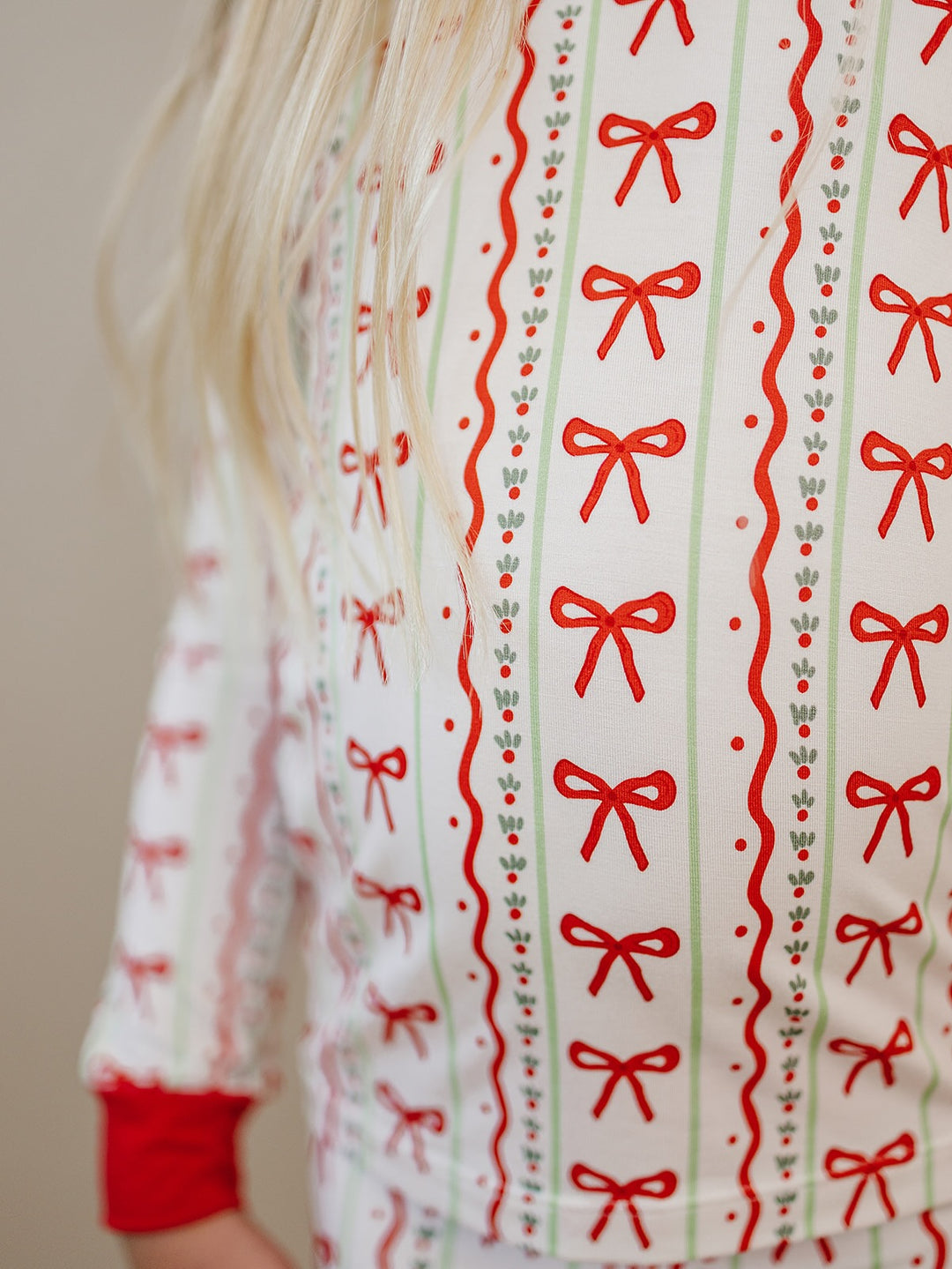 Close up of the Christmas Bows pajama top showing rows of red bows and festive stripes on a cream background.