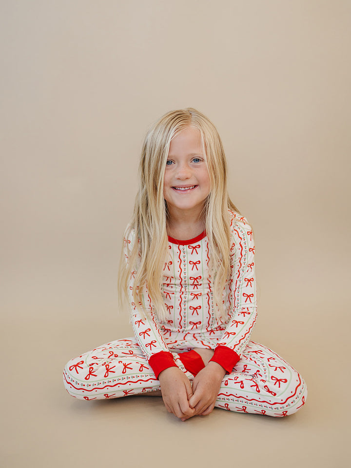 Smiling child sitting on the floor with legs crossed while wearing Christmas Bows two piece pajamas.