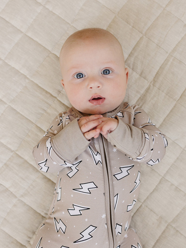 Baby lying on a cream quilt in the Latte Bolts bamboo zip romper in a close-up front view.