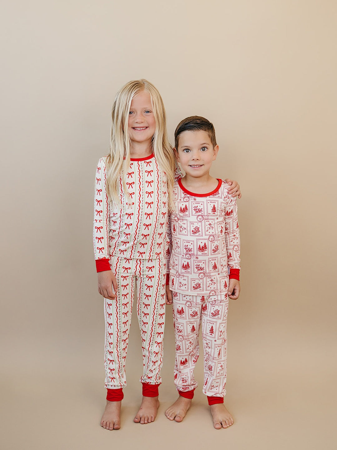 Two children standing together in Christmas Bows and North Pole Stamps Christmas pajamas.