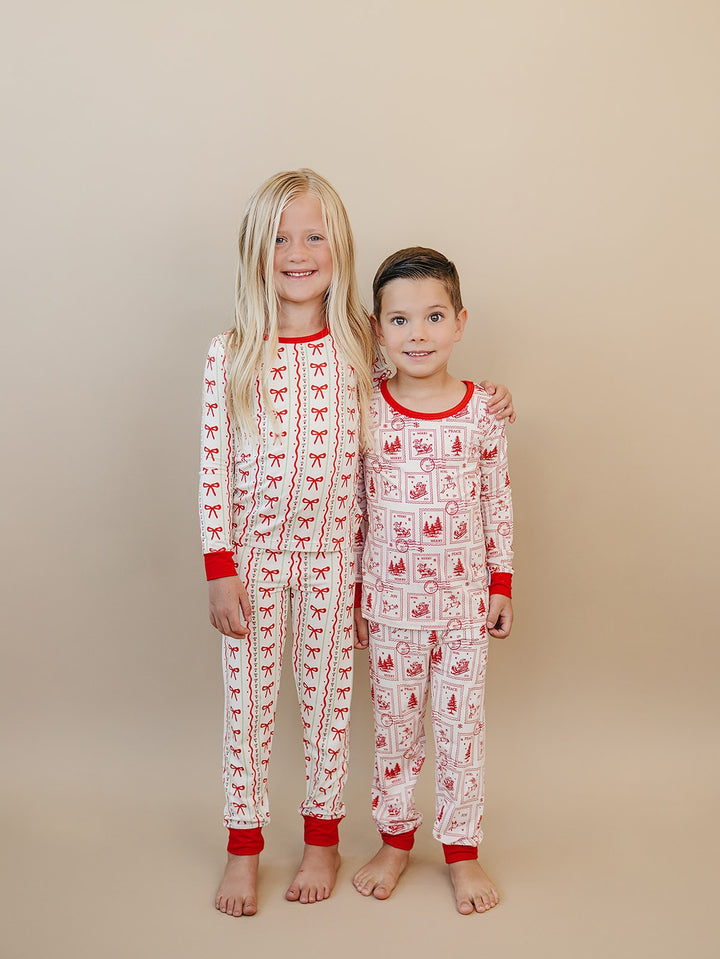 Two children standing together in Christmas Bows and North Pole Stamps Christmas pajamas.