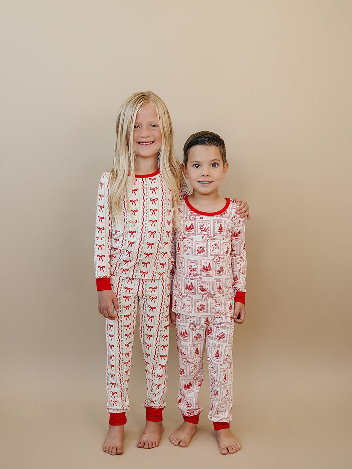 Children standing side by side in Christmas Bows and North Pole Stamps pajamas with matching red trim.