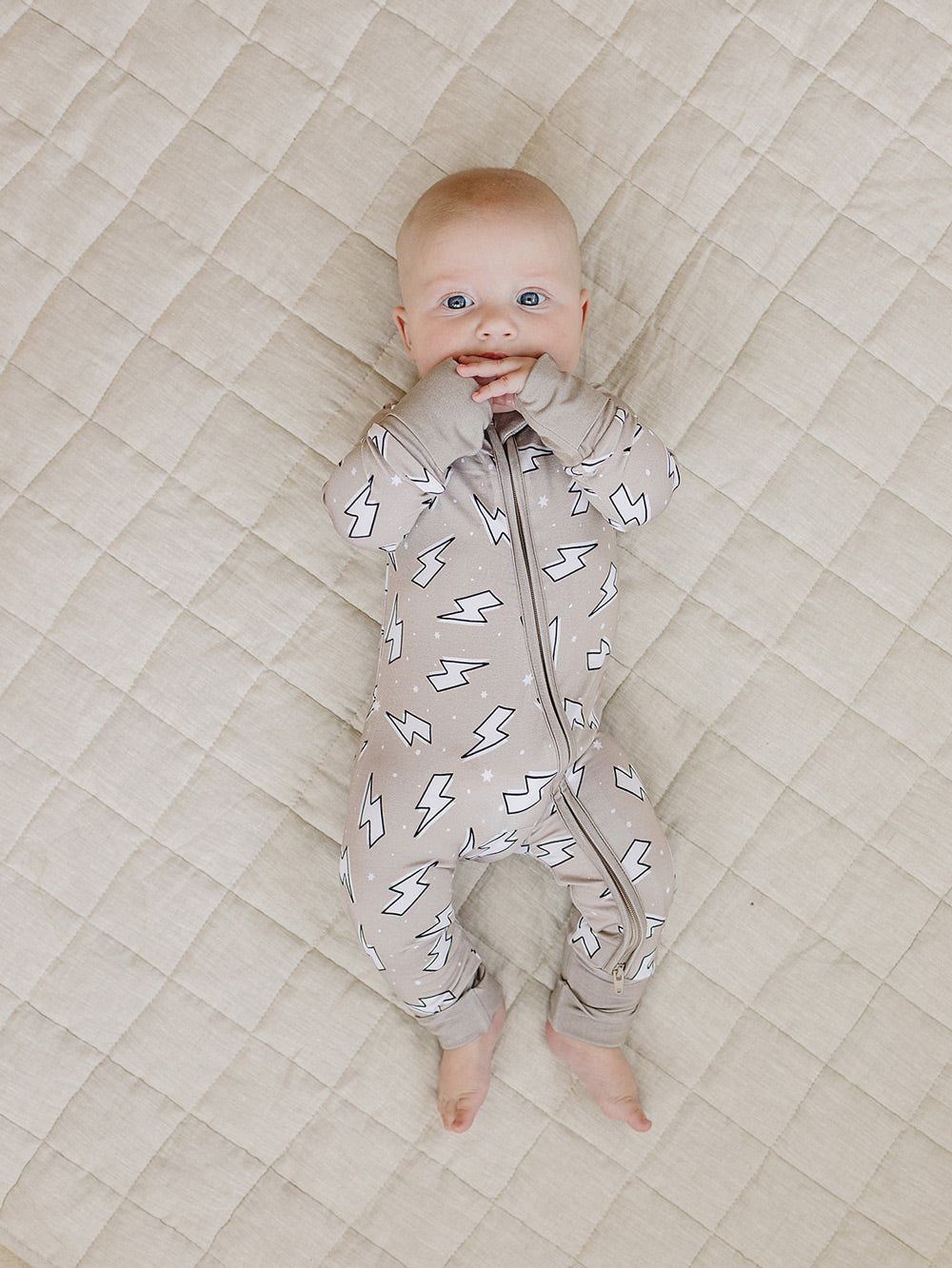Baby lying with arms raised in the Latte Bolts bamboo zip romper on a quilted blanket.