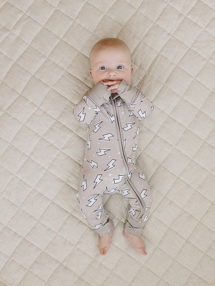 Baby lying with arms raised in the Latte Bolts bamboo zip romper on a quilted blanket.