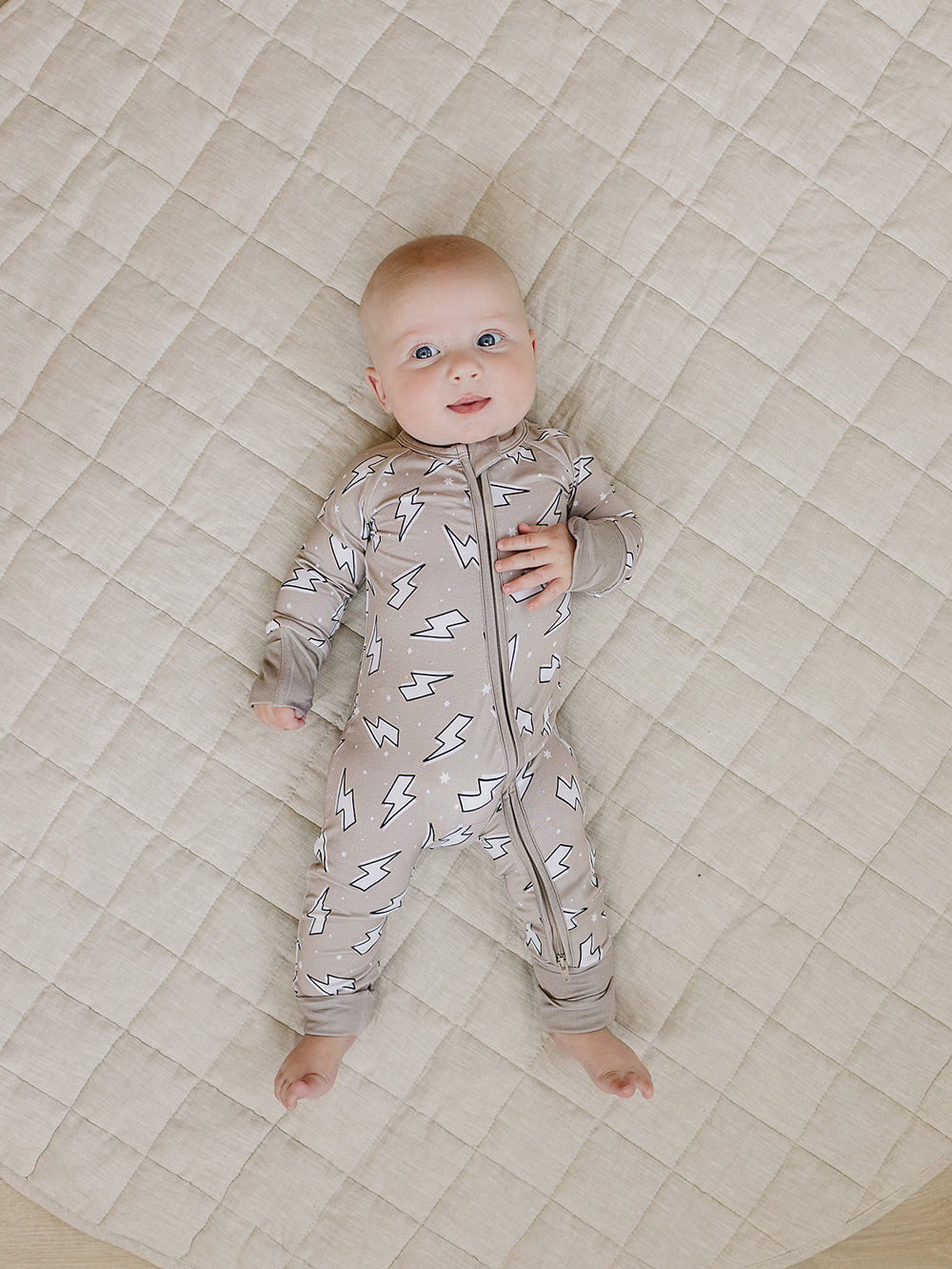 Baby lying comfortably on a quilt in the Latte Bolts bamboo zip romper, showing the front fit.