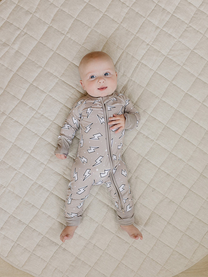 Baby lying comfortably on a quilt in the Latte Bolts bamboo zip romper, showing the front fit.
