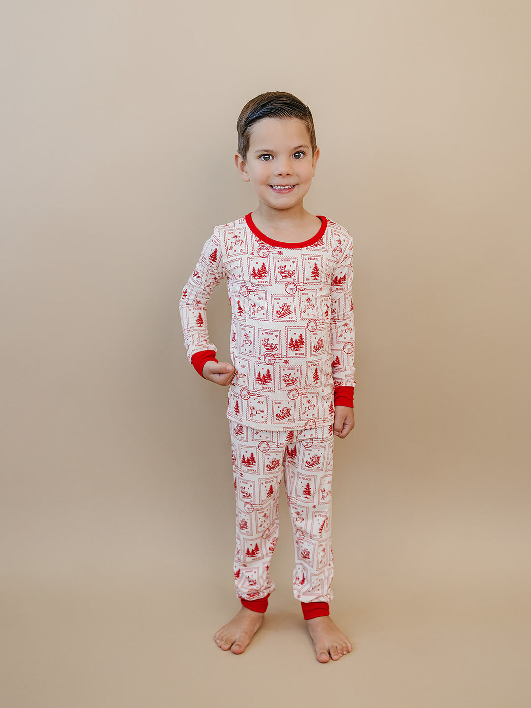 Child standing barefoot in North Pole Stamps pajamas, showing the long sleeve top and full length pants.