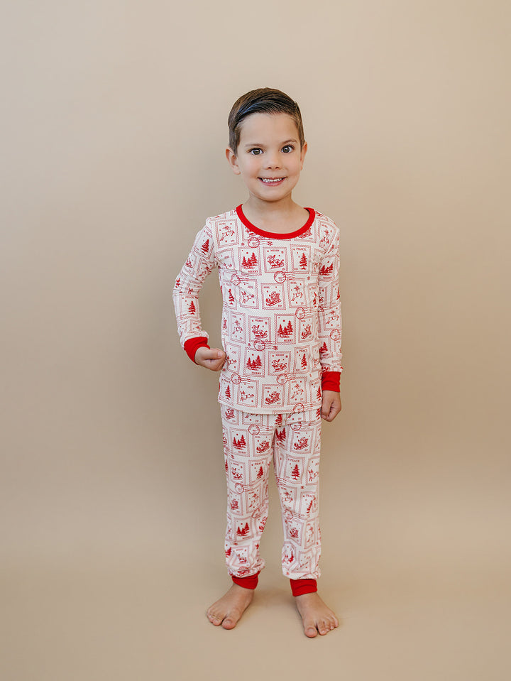 Child standing barefoot in North Pole Stamps pajamas, showing the long sleeve top and full length pants.