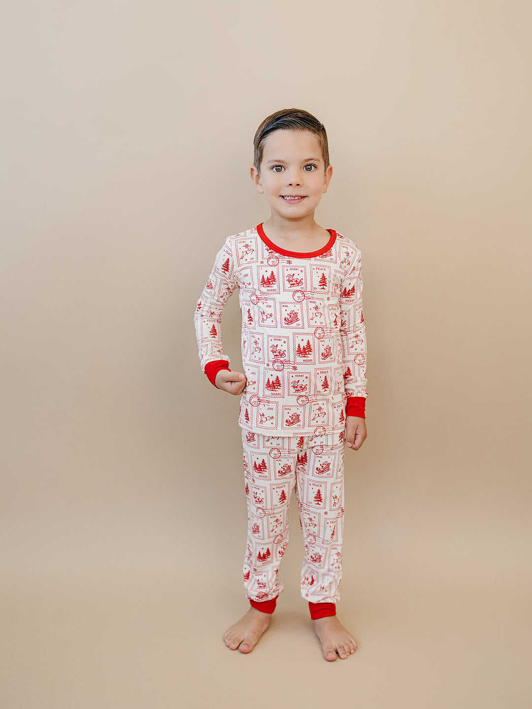 Front view of a child in the North Pole Stamps Christmas pajama top and matching red cuffed pants.