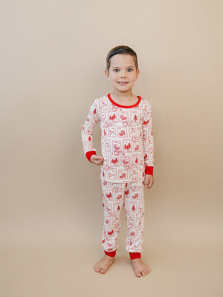 Front view of a child in the North Pole Stamps Christmas pajama top and matching red cuffed pants.