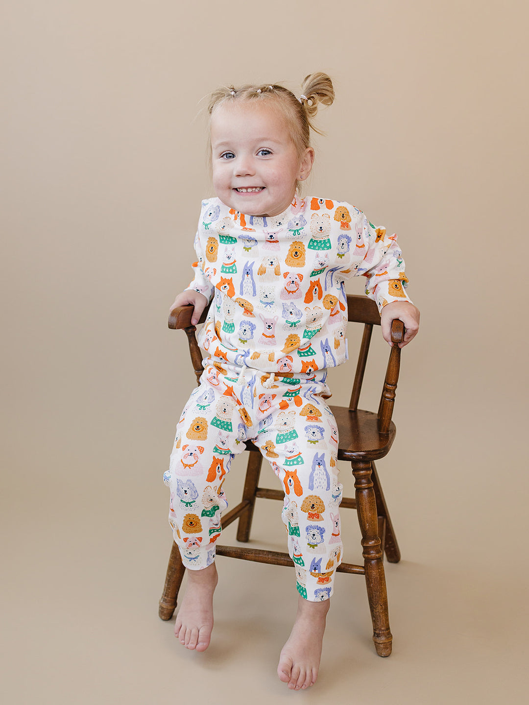 Toddler sitting on a wooden chair in the Puppy Club dog-print cotton top and matching jogger pants.