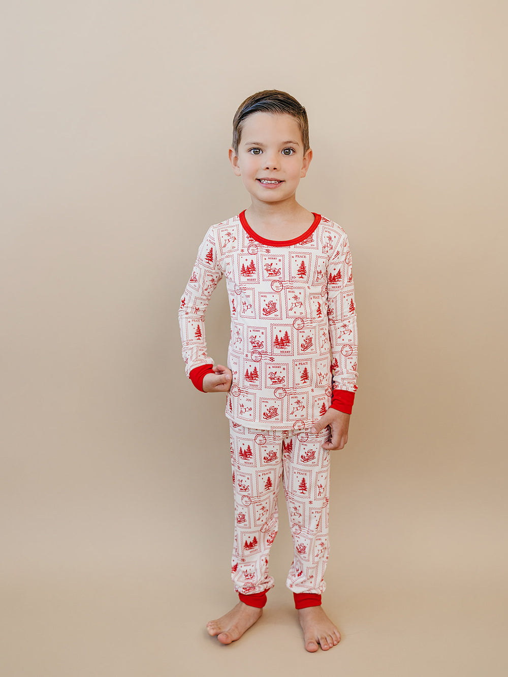 Child wearing the North Pole Stamps two piece Christmas pajamas with red neckline, wrist cuffs and ankle cuffs.