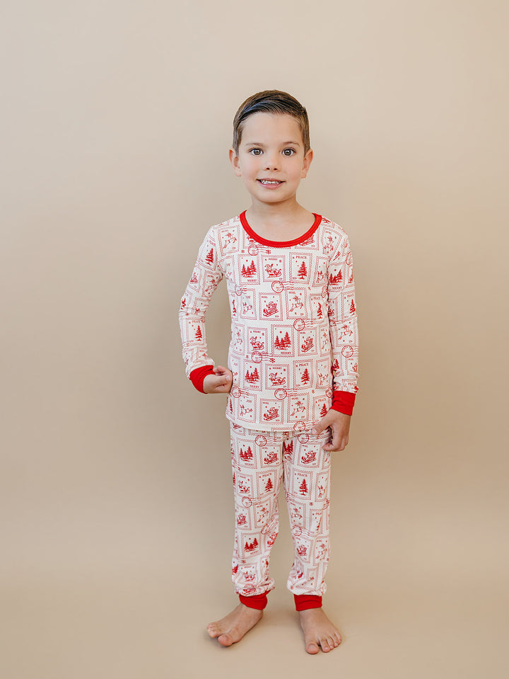 Child wearing the North Pole Stamps two piece Christmas pajamas with red neckline, wrist cuffs and ankle cuffs.