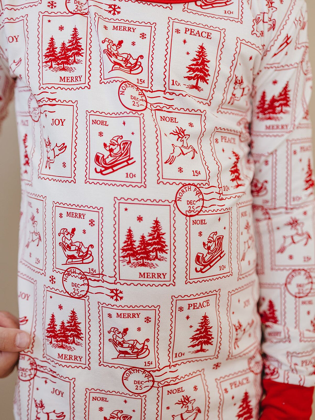 Close up of North Pole Stamps pajamas with red Santa, reindeer and Christmas tree stamps on a cream background.
