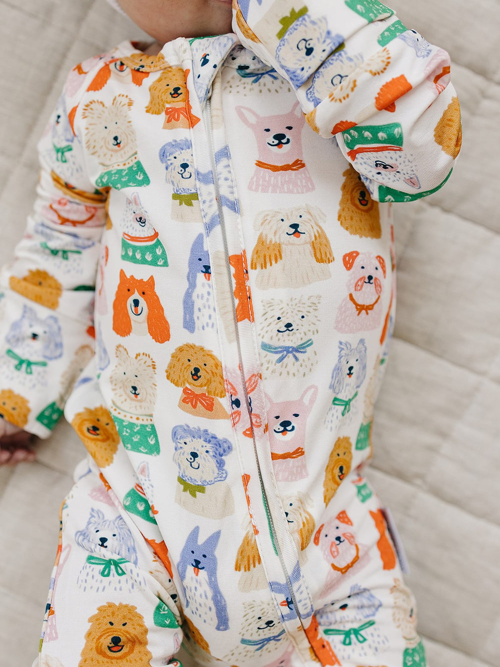 Close-up of the colorful dog print and front zipper on a baby’s Puppy Club bamboo romper.