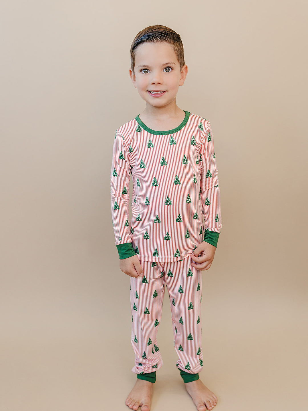 Front view of a child wearing the complete Magical Trees Christmas pajama set with green trim.