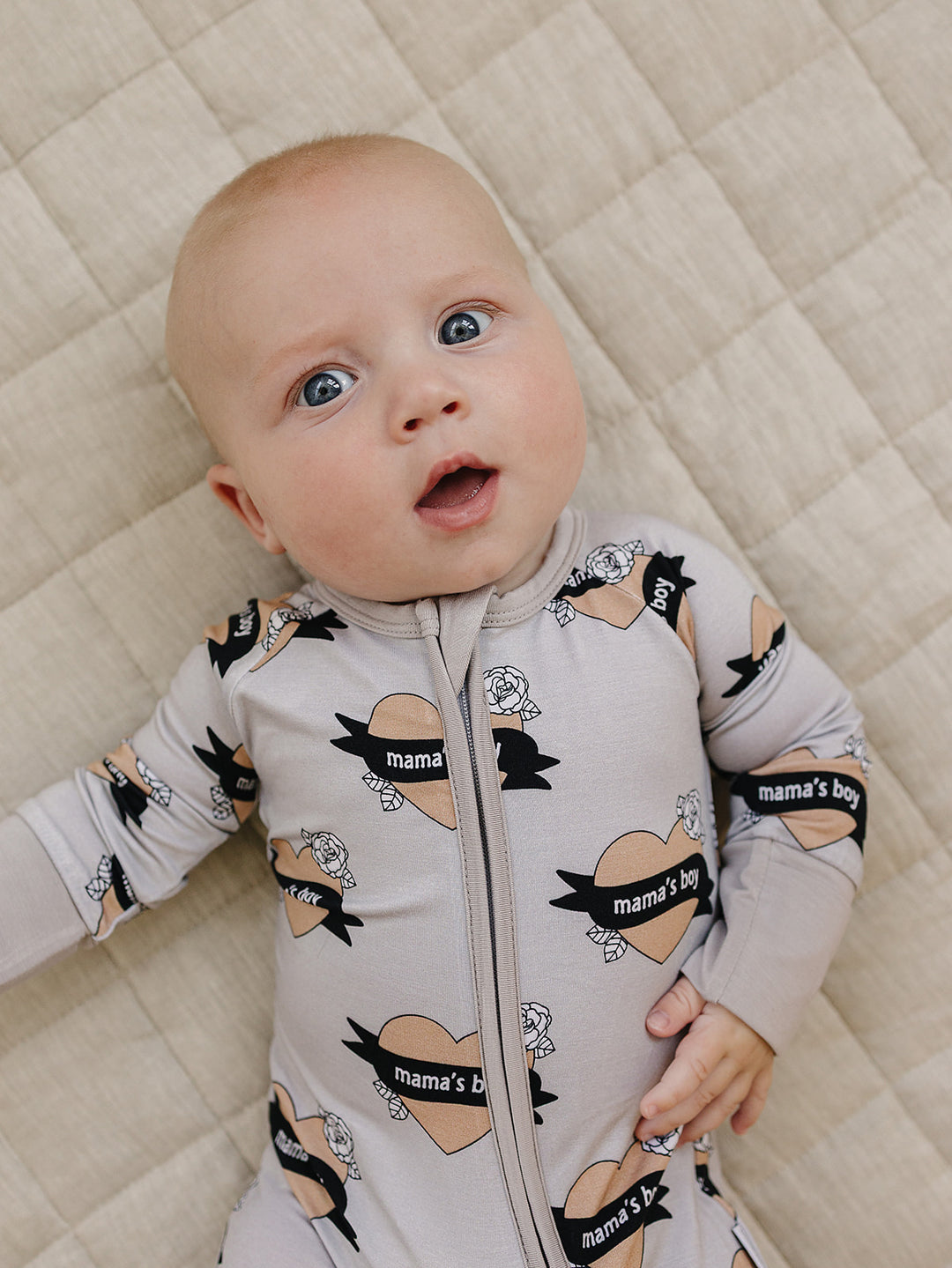 Baby looking toward the camera in the Mama’s Boy heart-print bamboo zip romper.
