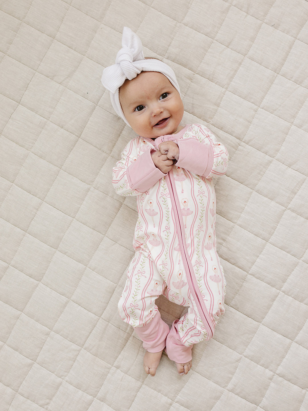 Full-length view of a baby wearing the Little Ballerina bamboo romper on a cream quilt.