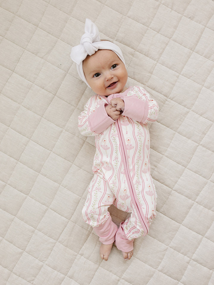 Full-length view of a baby wearing the Little Ballerina bamboo romper on a cream quilt.