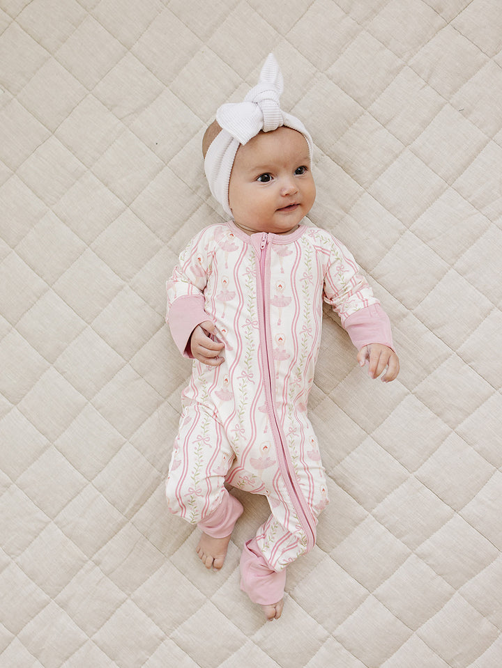 Full-length view of a baby modeling the Little Ballerina bamboo zip romper on a quilted mat.