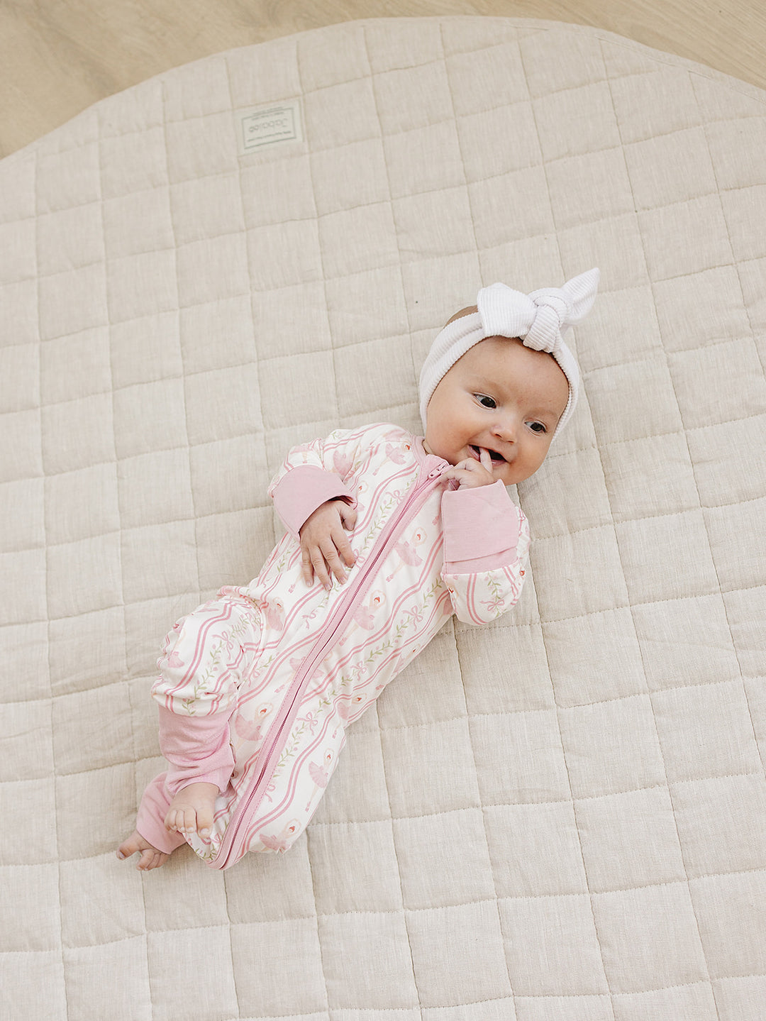 Baby lying on a cream quilt in the Little Ballerina bamboo zip romper.