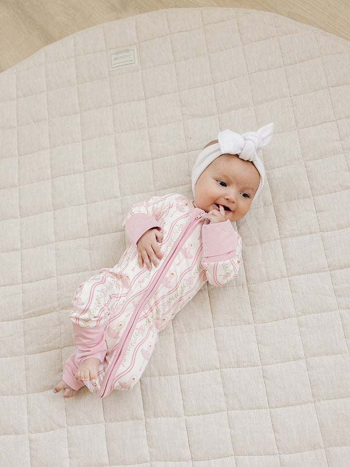 Baby lying on a cream quilt in the Little Ballerina bamboo zip romper.