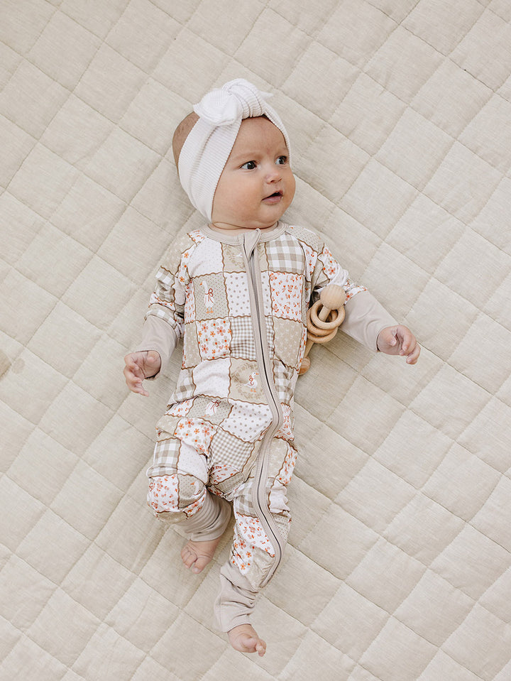 Full-body view of a baby lying on a cream quilt in the Cottage Goose bamboo zip romper.