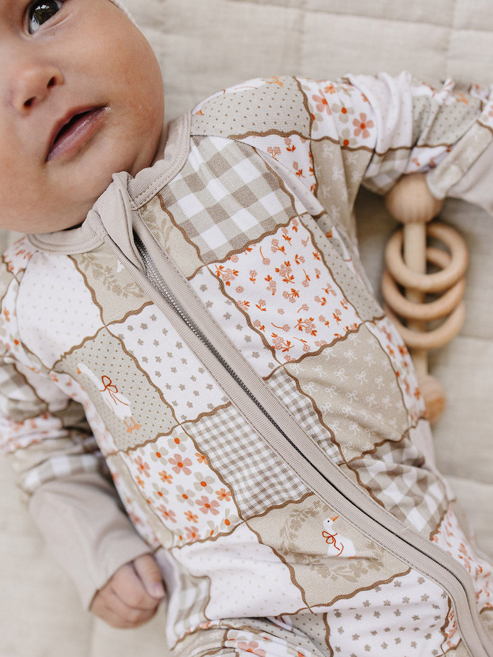 Close-up of a baby lying beside a wooden teething toy while wearing the Cottage Goose bamboo zip romper.