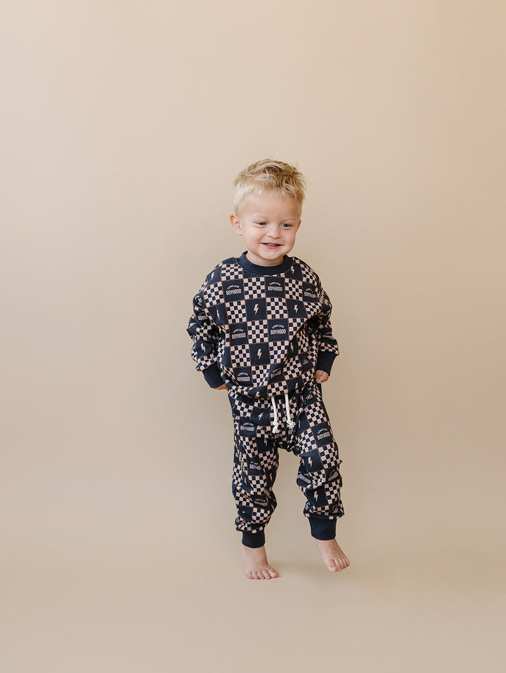 Smiling toddler standing in the Long Live Boyhood charcoal and beige cotton jogger set.