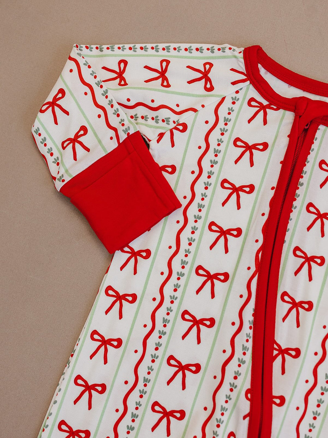 Detail of the Christmas Bows romper laid flat, showing the red neckline, sleeve cuff, zipper and bow print.